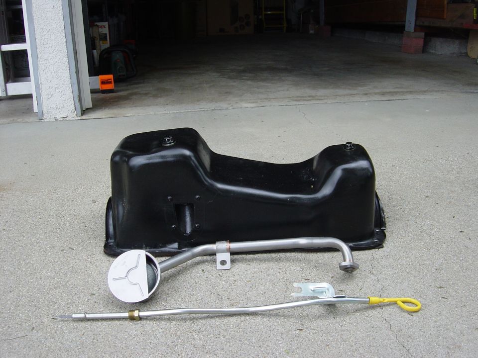 Black oil pan and metal dipstick with yellow handle on concrete
