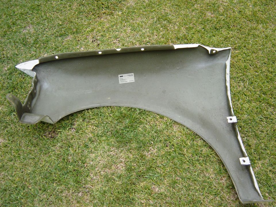 Inside of a white car fender, possibly fiberglass, lying on grass. Has a sticker on the inside