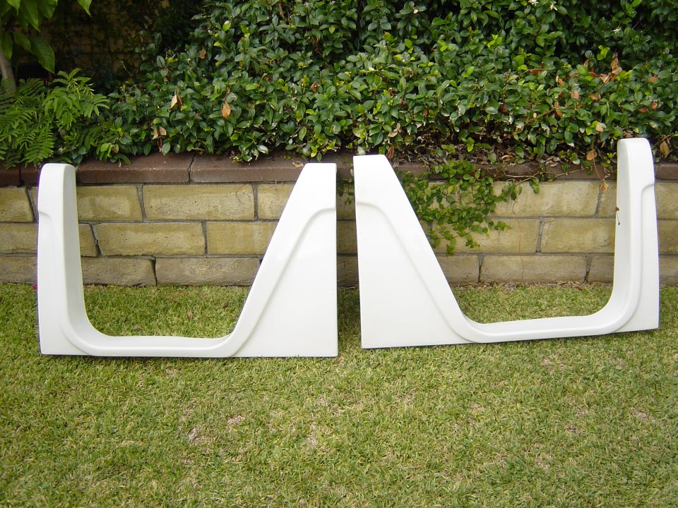 Two white car doors with cutouts, resting on grass in front of a brick wall and bushes
