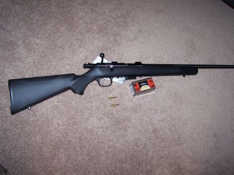 1995 Ford C-350 (Centurion Conversions) - A black rifle with a box of ammunition and two loose cartridges are displayed on a carpeted surface.