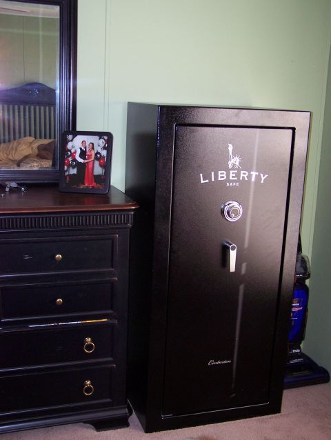 1995 Ford C-350 (Centurion Conversions) - A large black safe is positioned next to a dark dresser, with a framed picture on top of the dresser.