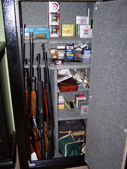 1995 Ford C-350 (Centurion Conversions) - A gun safe is open, revealing rifles stored vertically and various boxes of ammunition on shelves.
