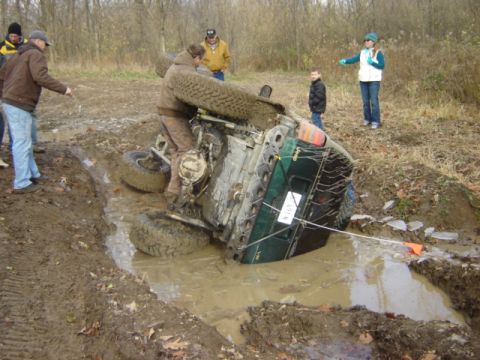1992 Ford Bronco - A group of people observe a Jeep Wrangler that has overturned in a muddy off-road area.