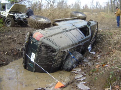 1992 Ford Bronco - Off-roading gone wrong: A Ford Bronco is stuck and overturned in the mud, with a Jeep assisting.