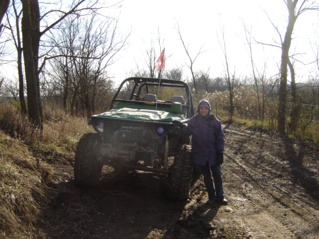 Person next to green Suzuki Samurai with large tires on a muddy trail