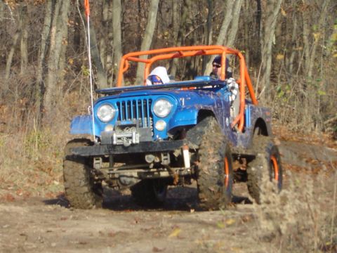 1992 Ford Bronco - This modified off-road jeep navigates a muddy trail with its driver and passenger visible.
