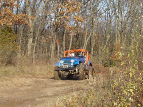 1992 Ford Bronco - A blue Jeep with an orange roll cage navigates a wooded trail during an off-road excursion.