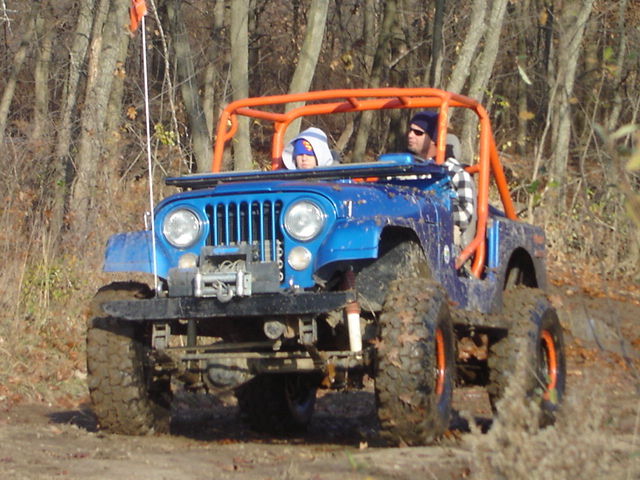 Blue Jeep with orange roll cage driving through mud, two people inside