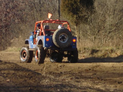1992 Ford Bronco - This modified off-road jeep navigates a dirt path, its orange roll cage and large tires clearly visible.