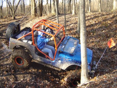1992 Ford Bronco - Off-road Jeep with orange roll cage navigating a muddy, wooded trail.