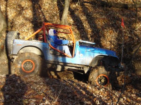 1992 Ford Bronco - This off-road vehicle, equipped with an orange roll cage, navigates a challenging, muddy trail covered in fallen leaves.