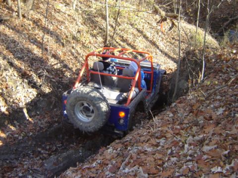 1992 Ford Bronco - Off-road Jeep Wrangler navigates a muddy trail surrounded by fallen autumn leaves.