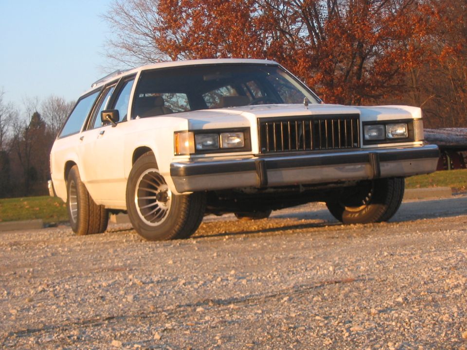 White station wagon with a vertical grille and quad headlights, parked on a gravel lot