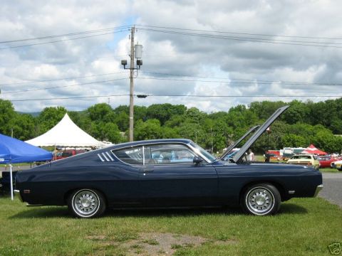 1969 Ford Torino - A dark blue 1969 Ford Torino coupe is parked on a grassy field with its hood open, showing the engine bay.