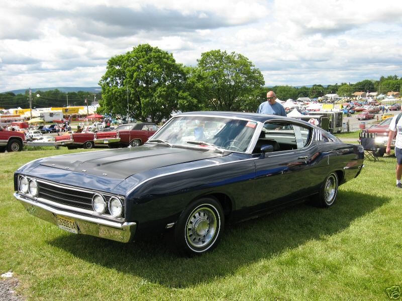 Dark blue 1968 Ford Torino coupe with chrome trim and white-letter tires, parked on grass at an outdoor event