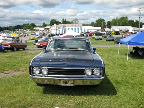 1969 Ford Torino - A blue 1969 Ford Torino is parked on a grassy field at an outdoor car show, with other vehicles and tents in the background.