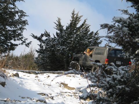 1995 Ford Bronco - A dark SUV navigates a snow-covered rocky path with trees on either side.