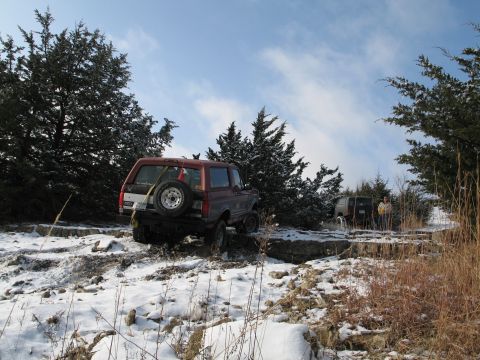 1995 Ford Bronco - A red Ford Bronco navigates a snowy, rocky landscape with another vehicle visible in the background.