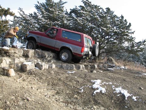 1995 Ford Bronco - A two-tone Ford Bronco navigates a rocky incline during an off-road excursion in winter conditions.
