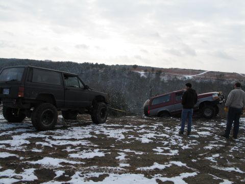 1995 Ford Bronco - Two SUVs are stuck in a snowy ditch, with one being pulled out by a tow strap.