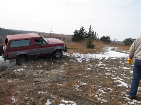 1995 Ford Bronco - Ford Bronco stuck on a muddy embankment with snow on the ground.