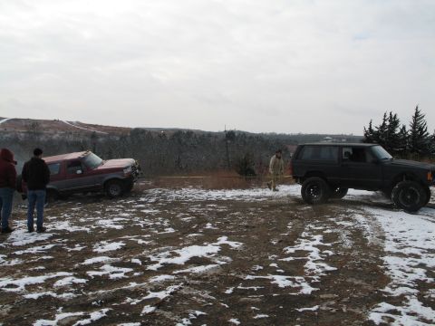 1995 Ford Bronco - Two SUVs are in a muddy, snowy area with trees and hills in the background under an overcast sky.