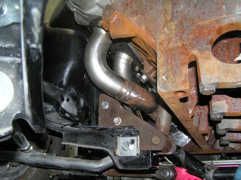 1964 Ford 427 - Underside view of a vehicle's engine block and exhaust system, showing new pipes and rusty metal.