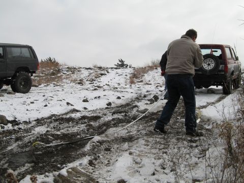 1995 Ford Bronco - Two vehicles are stuck in a snowy, muddy terrain as people attempt to tow one out.