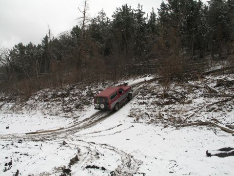 1995 Ford Bronco - A red and silver SUV navigates a snowy and muddy path through a wooded area.