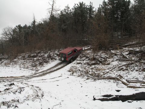 1995 Ford Bronco - A red 1995 Ford Bronco navigates a challenging snowy incline surrounded by trees and debris.