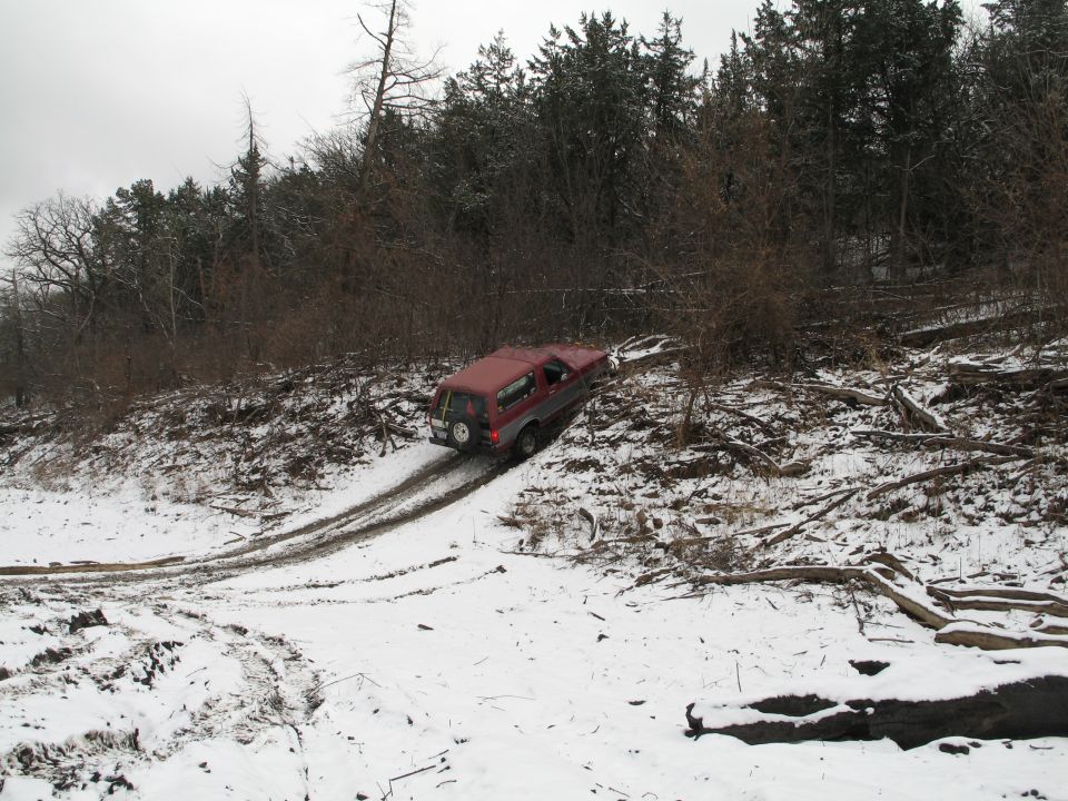 Red 1995 Ford Bronco driving on a snowy, wooded hill