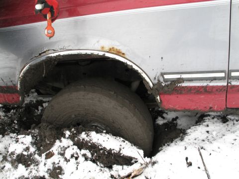 1995 Ford Bronco - A red and silver SUV is stuck in mud and snow, with its wheel deeply embedded.
