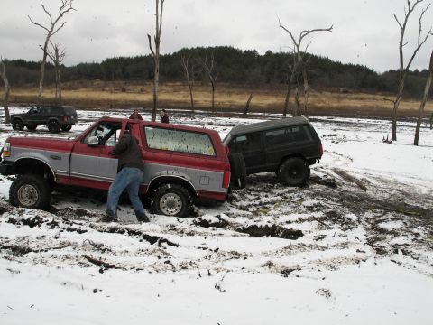 1995 Ford Bronco - A red and silver 1995 Ford Bronco is stuck in the mud and snow, with a black Jeep Cherokee behind it.