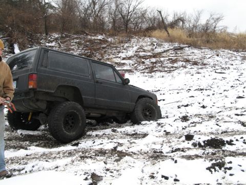 1995 Ford Bronco - A black SUV with off-road tires is stuck in a snowy, muddy embankment.