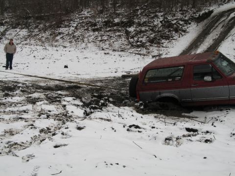 1995 Ford Bronco - Red 1995 Ford Bronco stuck in a muddy, snowy ditch, being pulled by a tow rope.