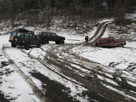 1995 Ford Bronco - A red and silver Ford Bronco is stuck in the mud and snow, with other vehicles nearby on a trail.