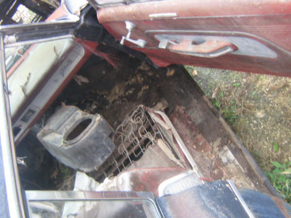 Car interior with torn upholstery, rusted metal, and debris on the floor
