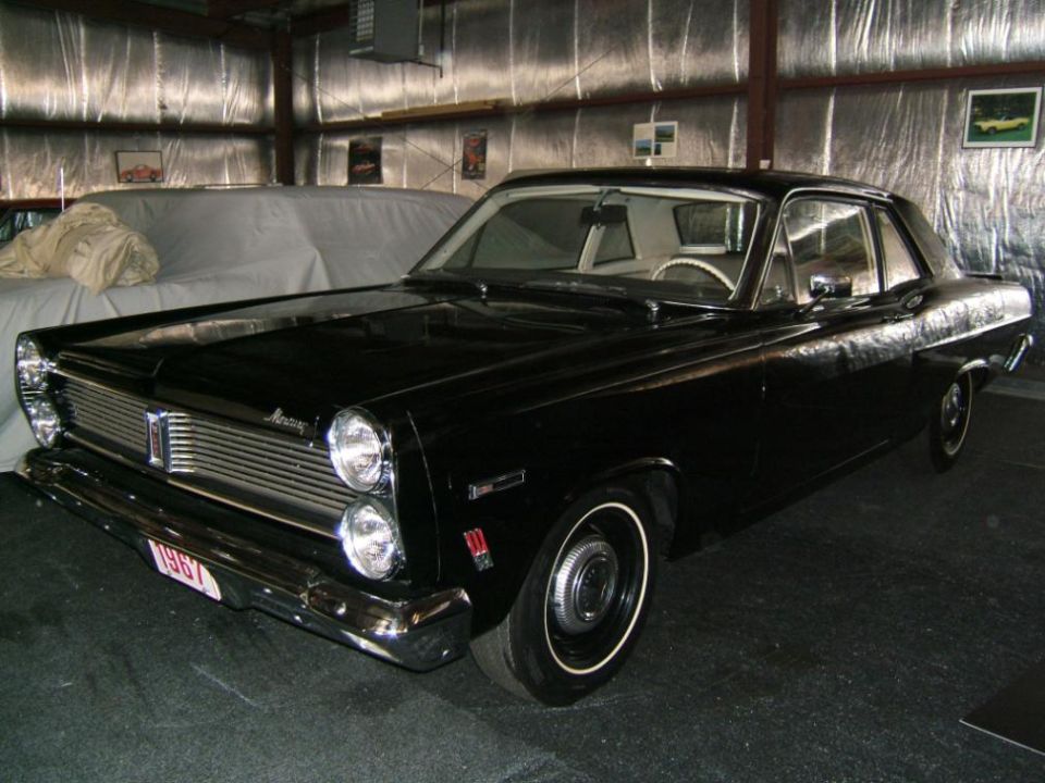Black 1967 Mercury two-door with whitewalls and 1967 front plate parked inside a metal garage