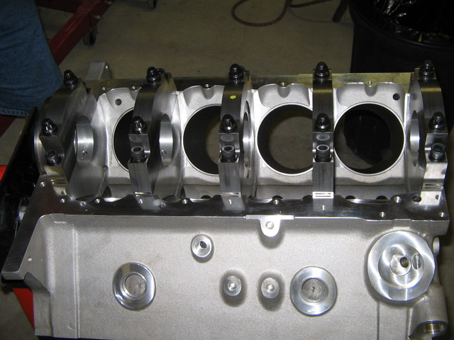 Bare aluminum V8 engine block with main bearing caps and studs on a bench