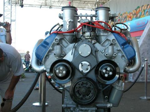 1968 Ford 427 - A V8 engine with dual carburetors and blue valve covers is displayed, with spectators in the background.