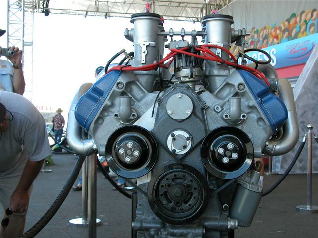 V8 engine with twin intake stacks, blue valve covers and red plug wires on a stand