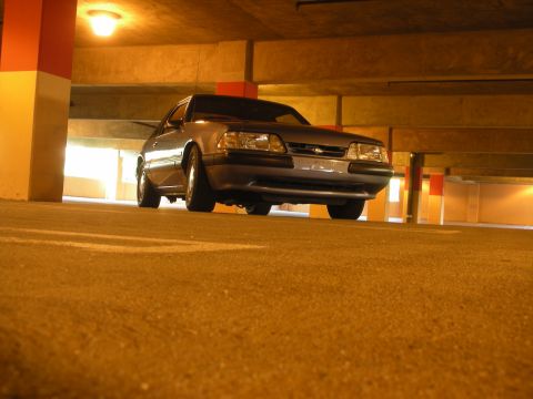 1990 Ford Mustang - A silver 1990 Ford Mustang is parked in a dimly lit parking garage, viewed from a low angle.