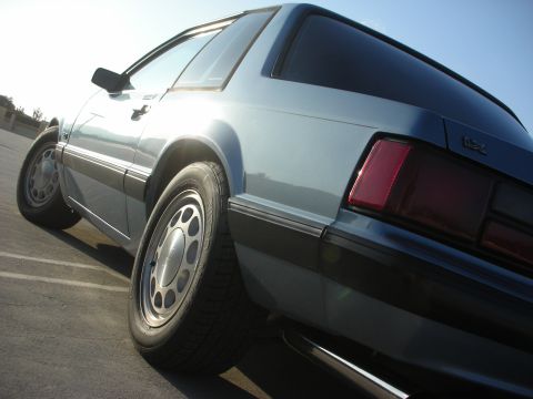 1990 Ford Mustang - The rear three-quarter view of a light blue 1990 Ford Mustang coupe is captured under a bright sky.