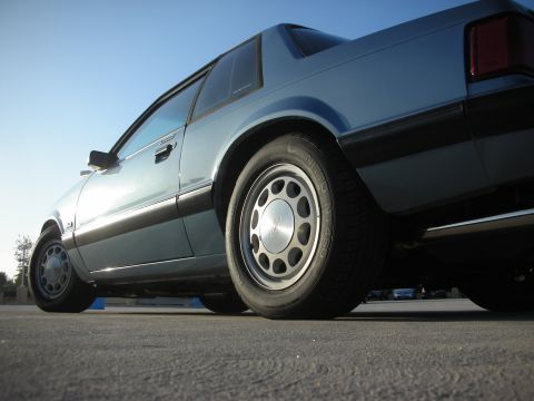 1990 Ford Mustang - A blue 1990 Ford Mustang coupe is shown from a low angle, highlighting its distinctive body style and wheels.