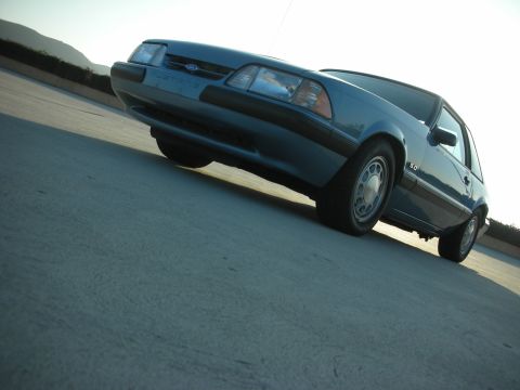 1990 Ford Mustang - A blue 1990 Ford Mustang is shown from a low angle, highlighting its front three-quarter view.