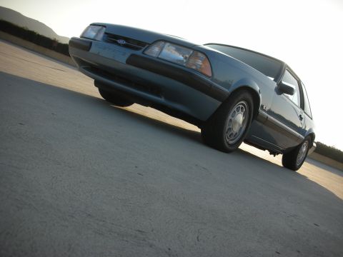 1990 Ford Mustang - A blue Ford Mustang coupe with a 5.0 badge is seen from a low angle on a concrete surface.