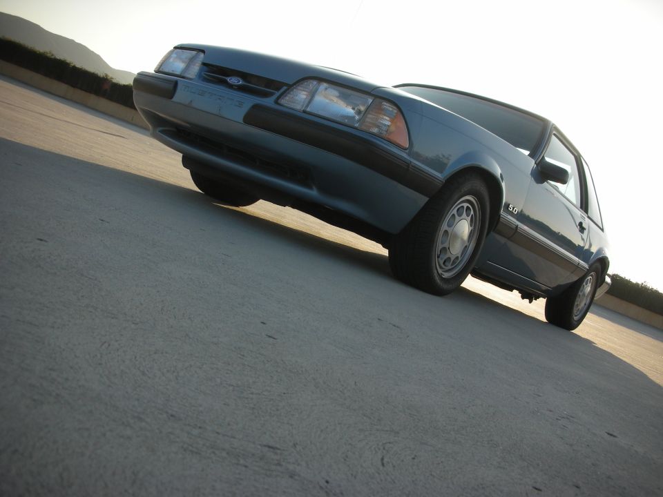 Blue Ford Mustang 5.0 coupe, front 3/4 view, low angle, parked on concrete