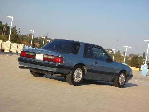 1990 Ford Mustang - A blue coupe is parked in an open area with a clear sky overhead.
