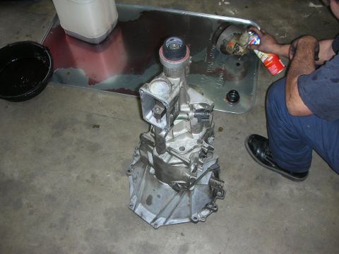 1990 Ford Mustang - A transmission assembly sits on a concrete floor while a person cleans a component in the background.