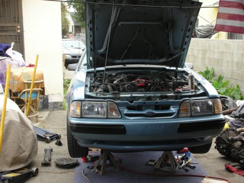 1990 Ford Mustang - Front view of a blue 1990 Ford Mustang with its hood open, parked on jack stands for maintenance.